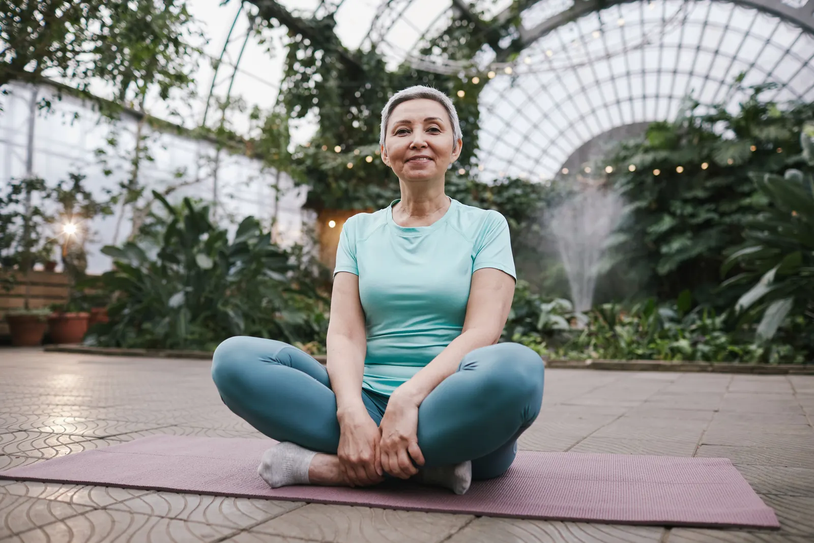 A woman seated on a mat in a bright glasshouse